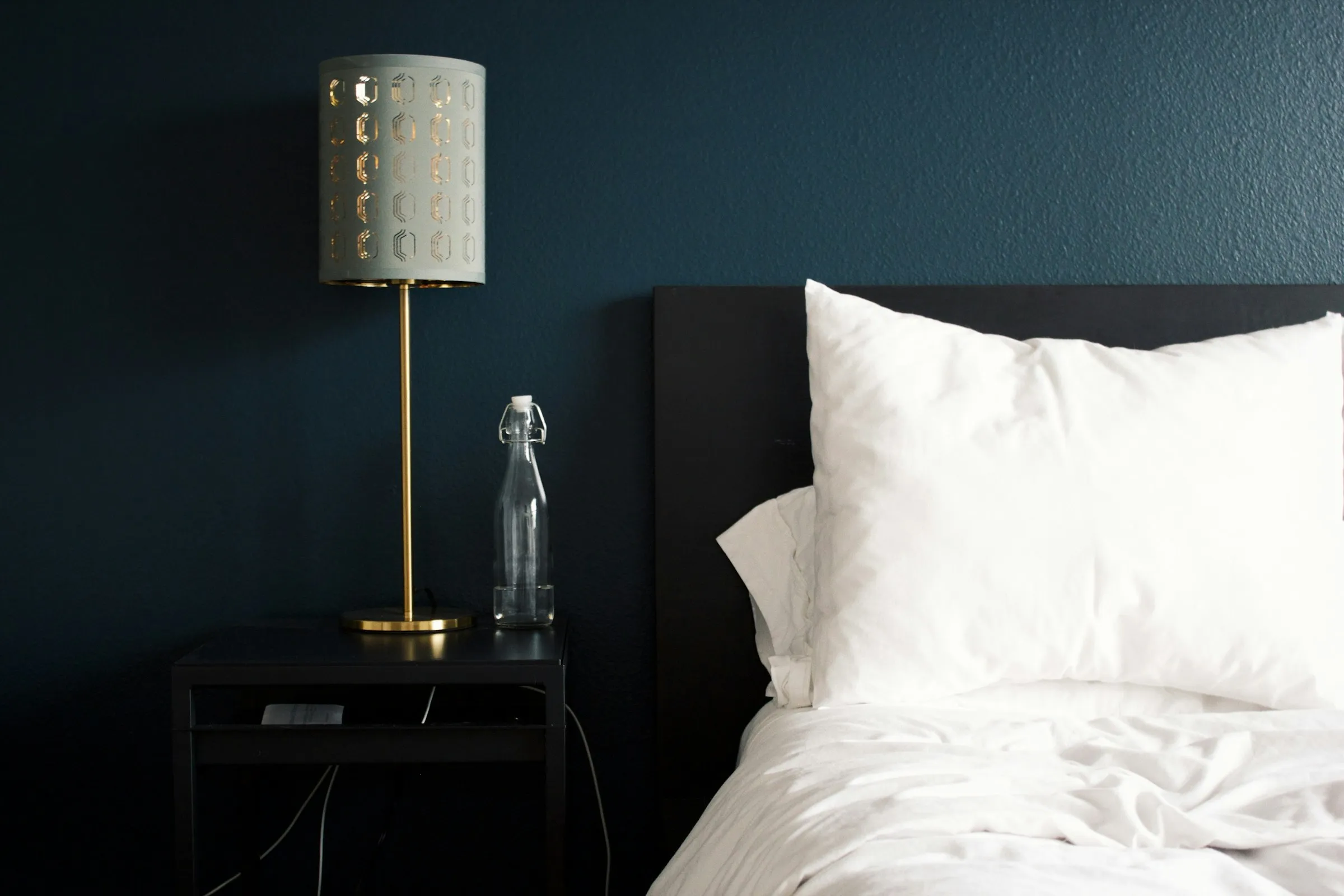 A made bed with a bedside lamp and water bottle in a rental