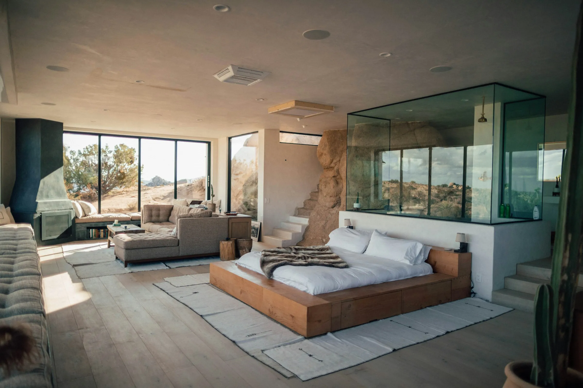 An apartment-style hotel suite with a bed, sofa and glass-walled bathroom