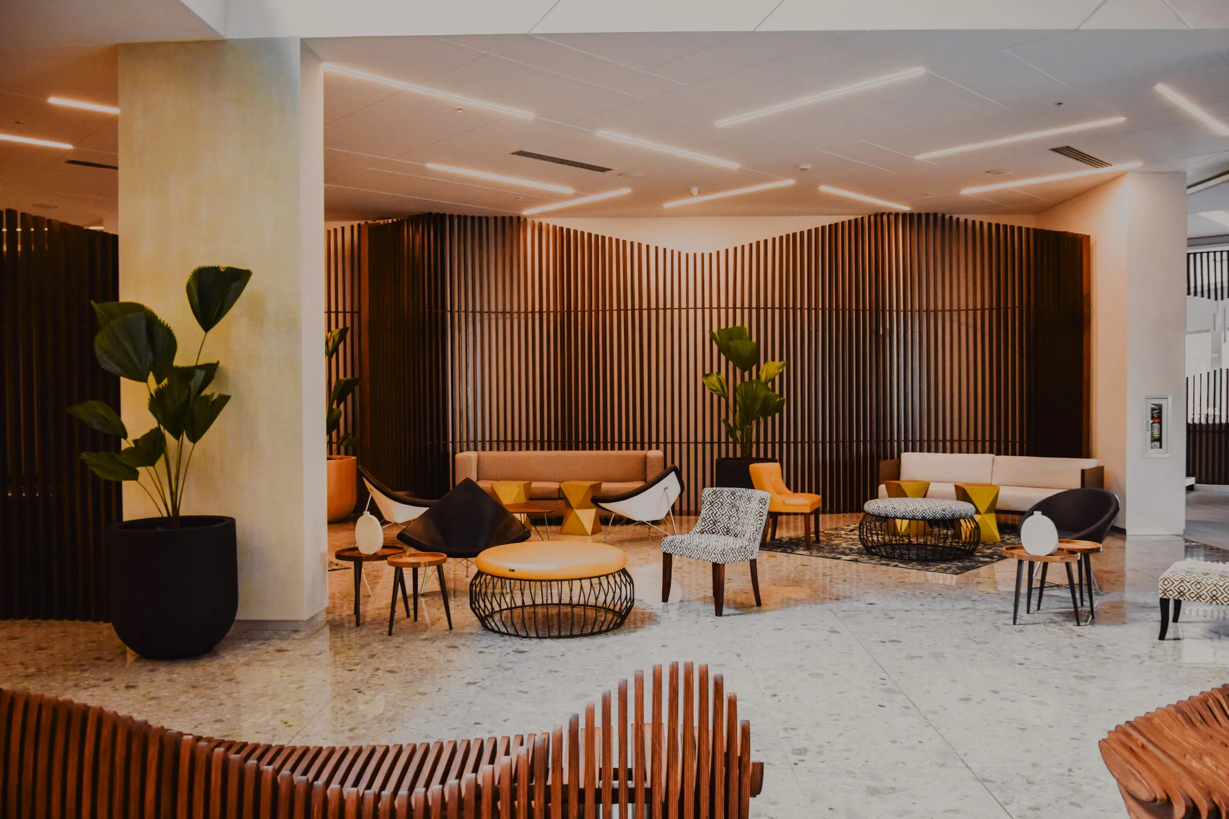 A hotel lounge with slatted wood walls, plants and low seating